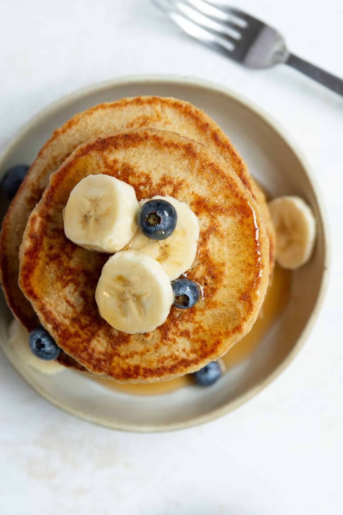 Overhead view of healthy protein oatmeal pancakes with crisp, buttery edges topped with banana and blueberries.