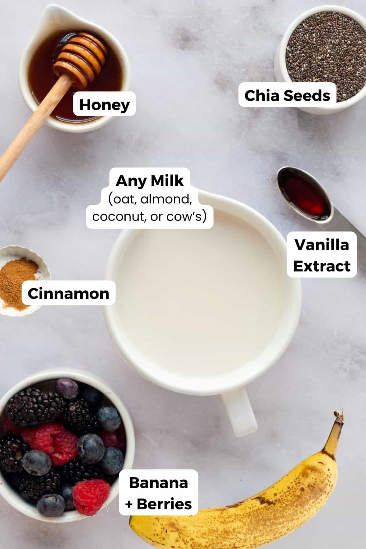All ingredients in banana chia seed pudding including: chia seeds, milk, vanilla extract, cinnamon, honey, banana, and berries.