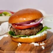 Super juicy Greek bison burger with feta, tzatziki, lettuce, tomato, and red onion on a brioche bun.