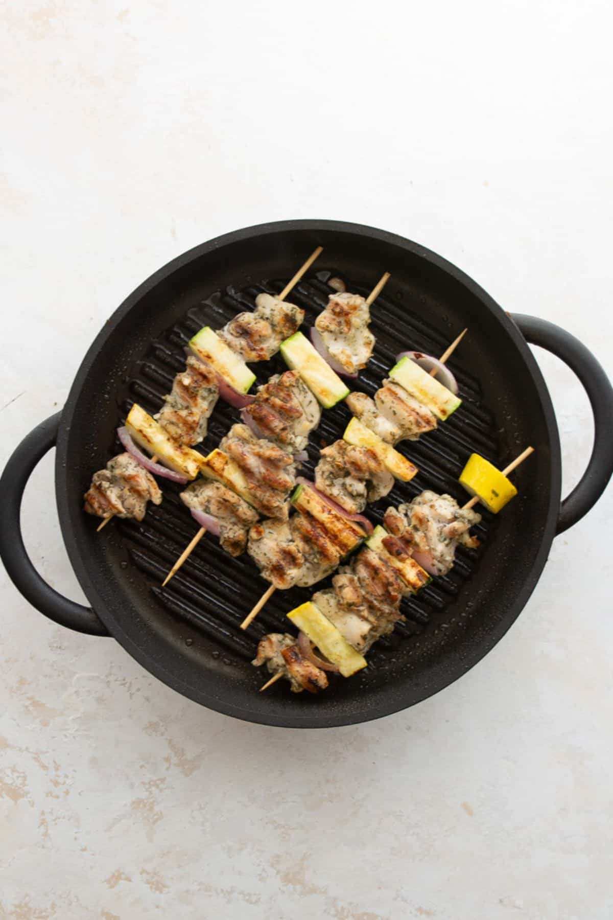 Greek chicken skewers grilling on a grill pan until golden and lightly charred.