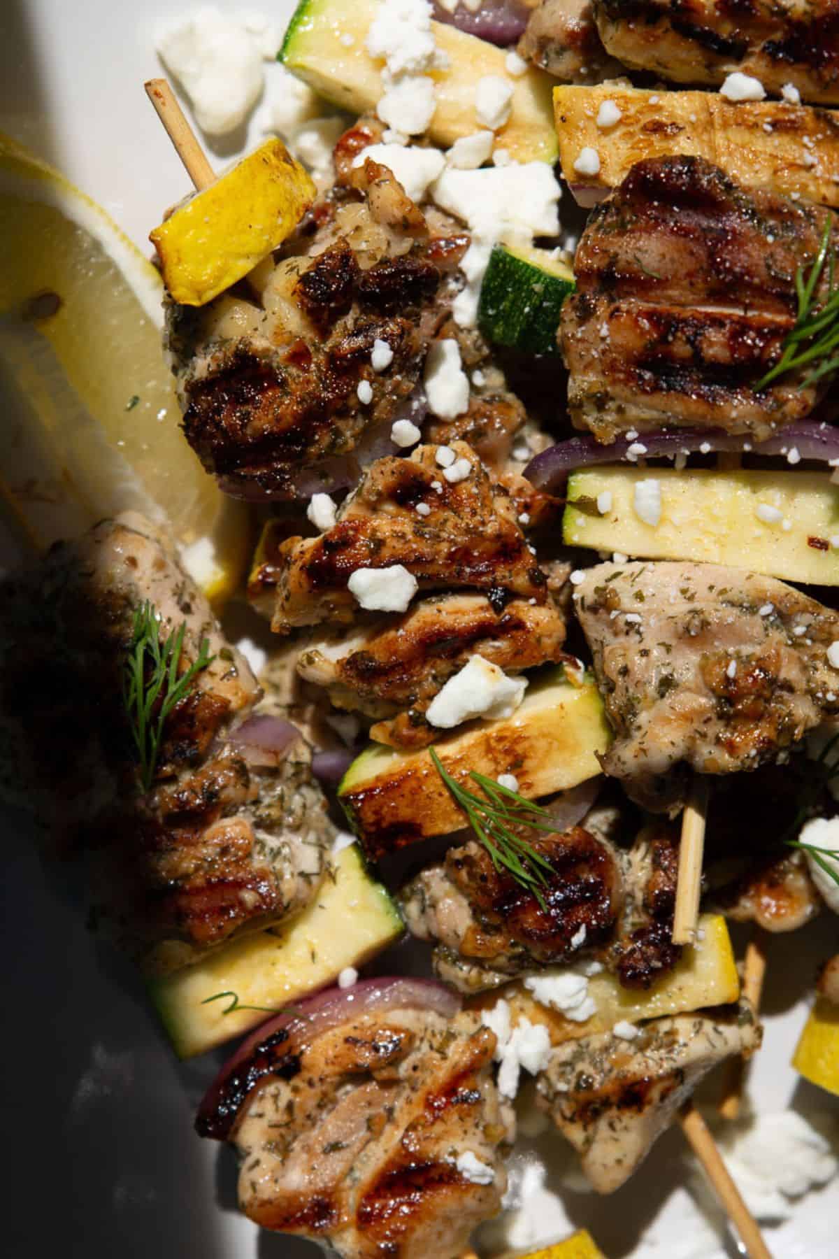 Juicy grilled Greek chicken kabobs with zucchini and red onion, garnished with feta and dill.