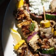 Juicy grilled Greek chicken kabobs with zucchini and red onion, served with a bowl of healthy tzatziki.