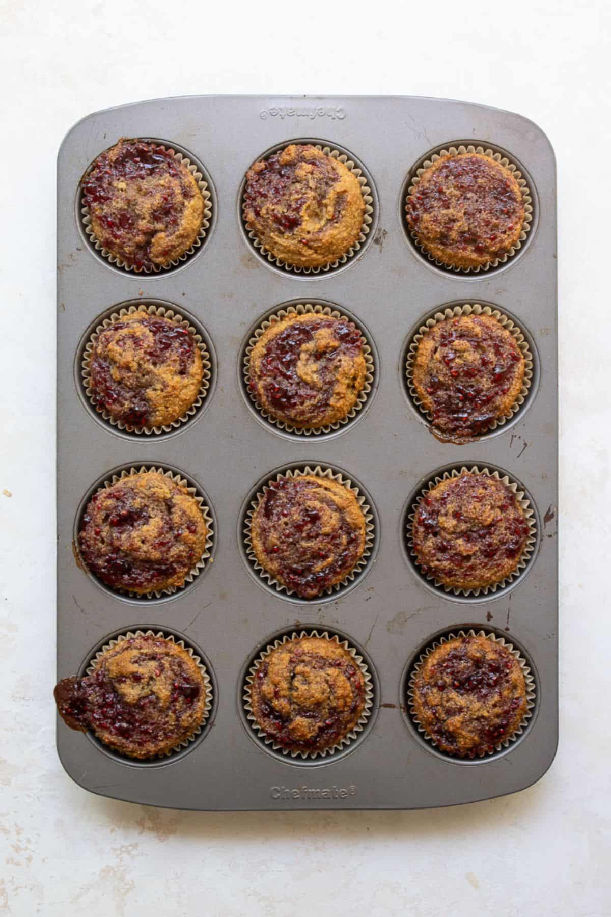 Baked healthy peanut butter and jelly banana muffins with golden tops and jam swirl.