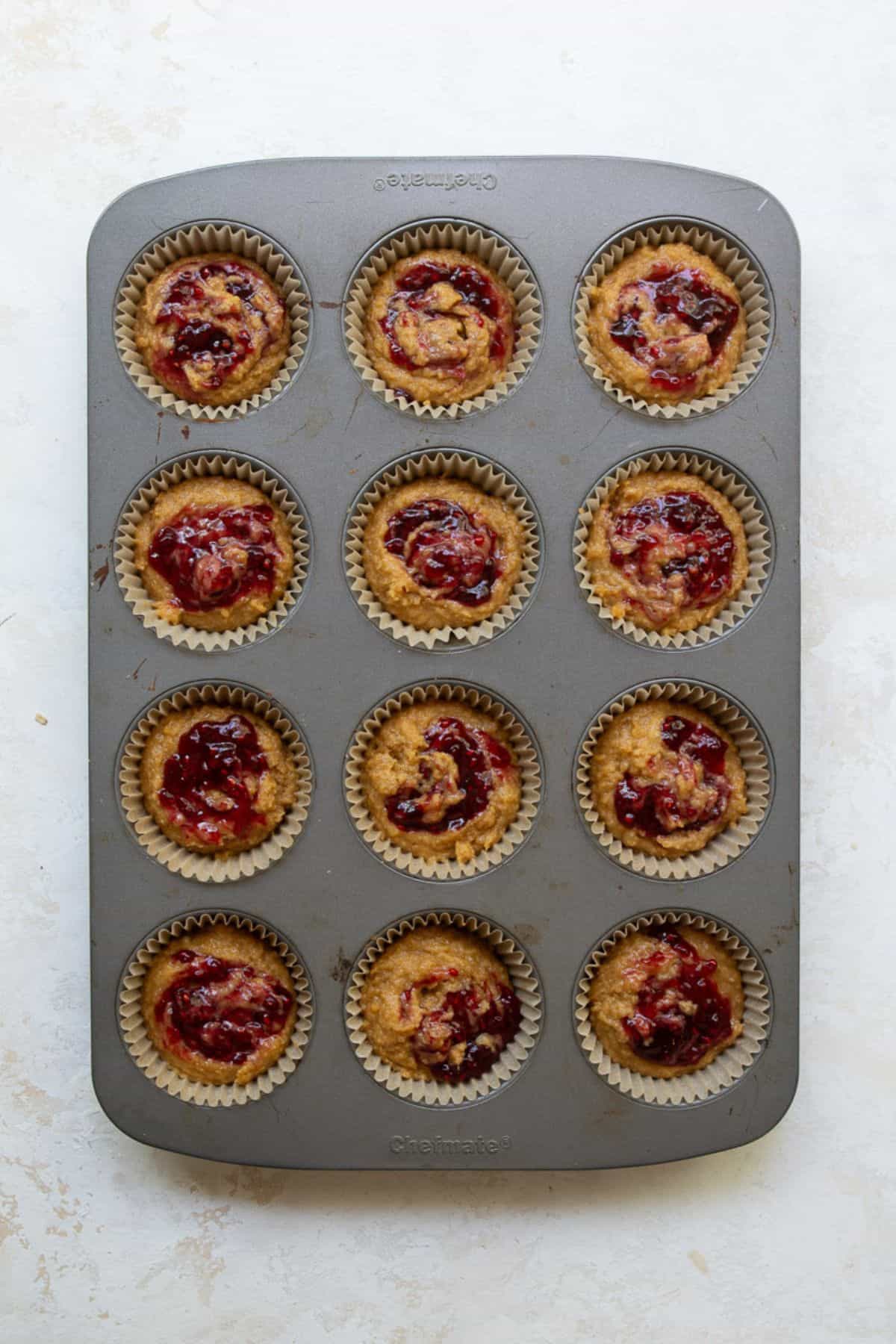 Raspberry jam swirled on top of gluten-free PB&J banana muffin batter before baking.