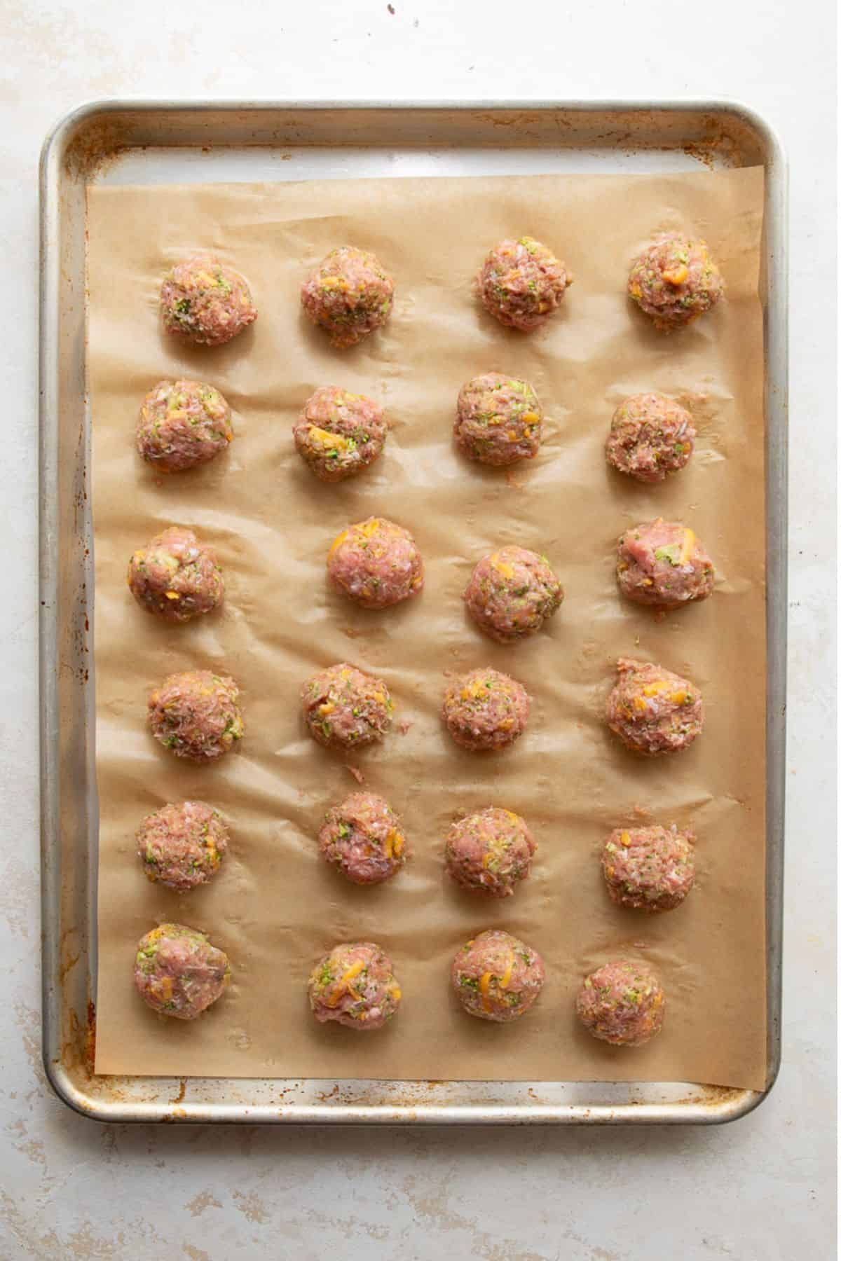 Raw broccoli cheddar turkey meatballs shaped and evenly spaced on a parchment-lined baking sheet before baking.