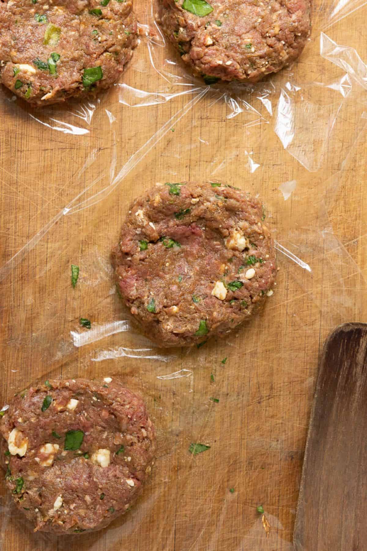Raw bison burger patties shaped on a wooden cutting board, one with a thumb dimple in the center.