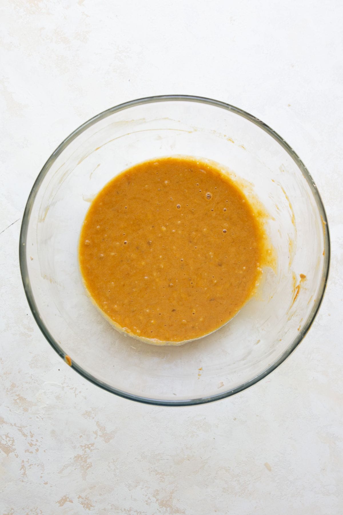 Peanut butter, banana, eggs and maple syrup whisked smooth in a glass bowl.