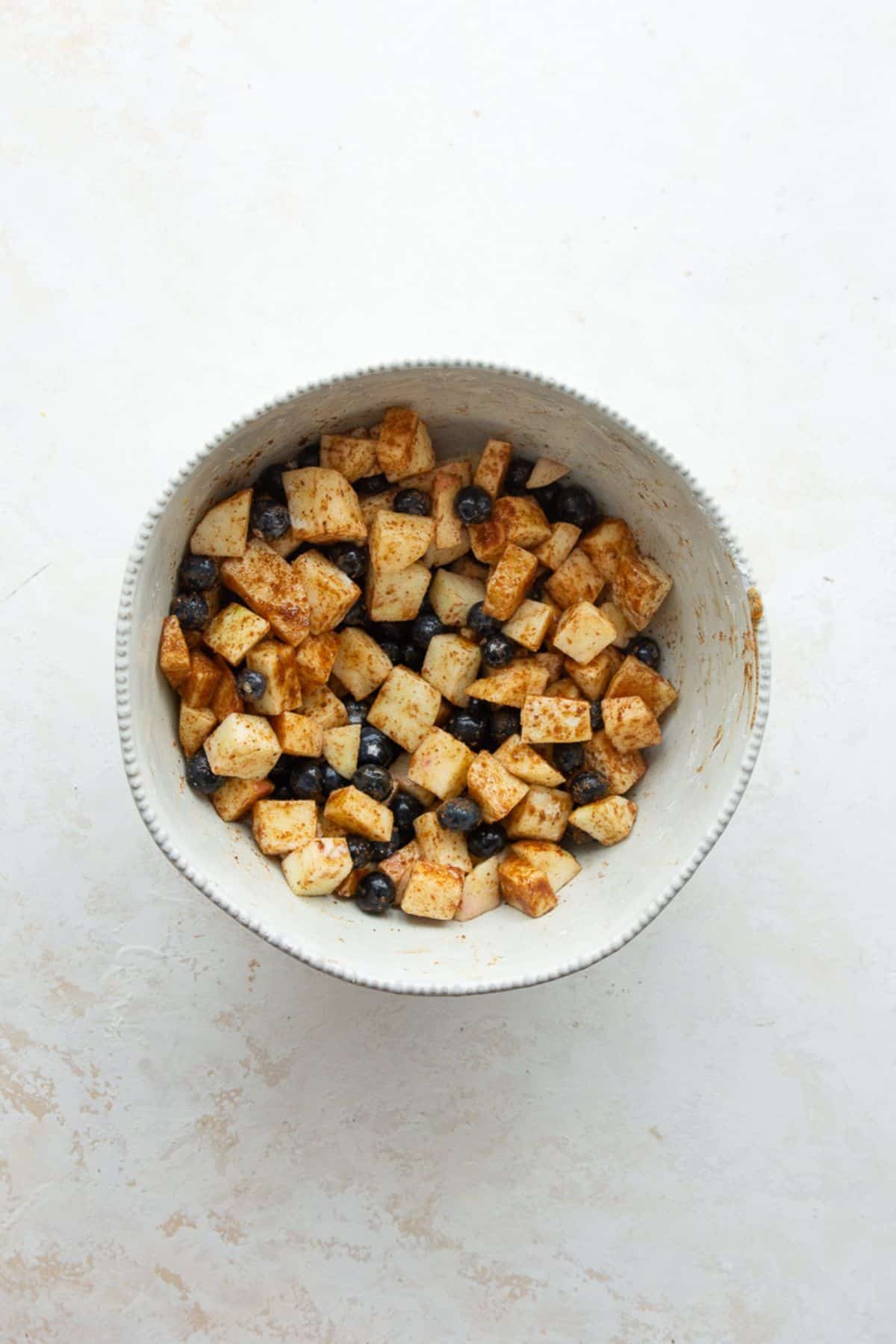 Diced apples and blueberries tossed with cinnamon and coconut sugar in a white bowl.