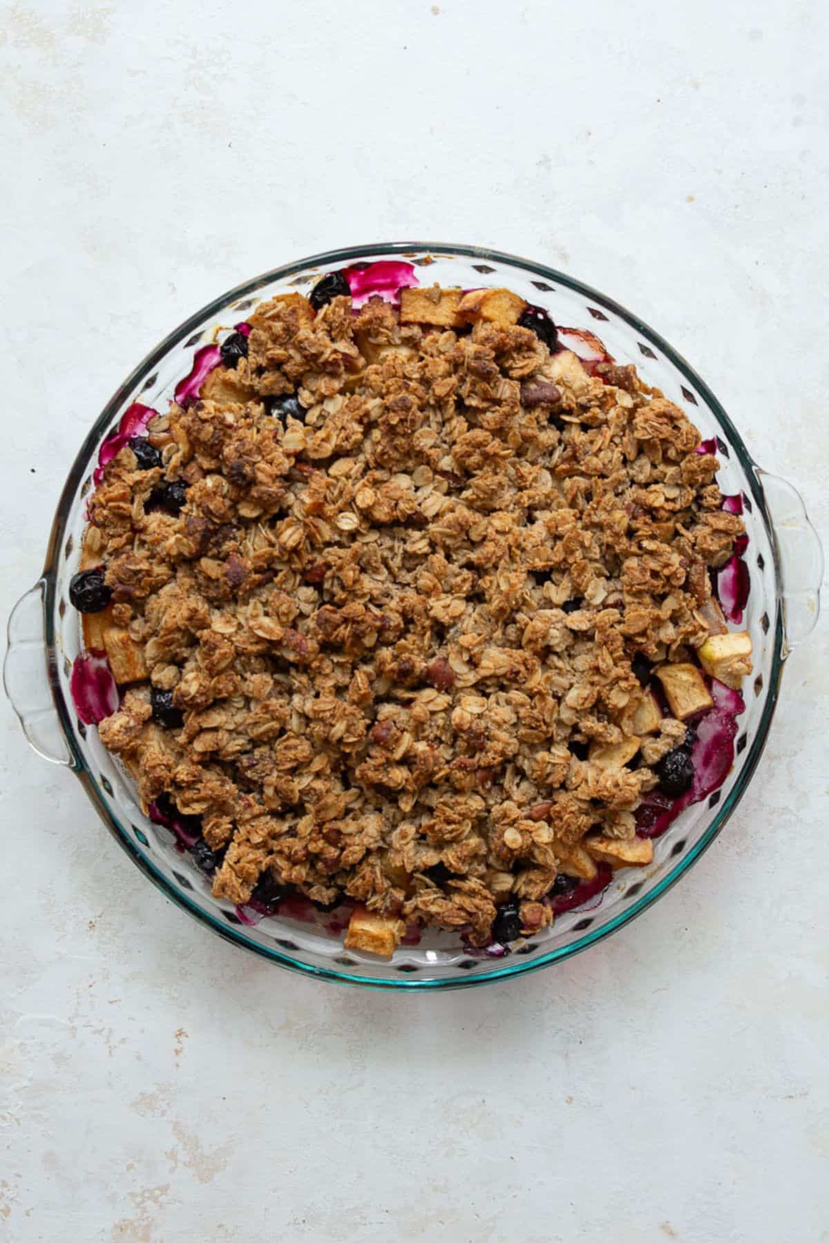 Golden baked apple blueberry crisp with bubbling fruit in a glass pie dish.