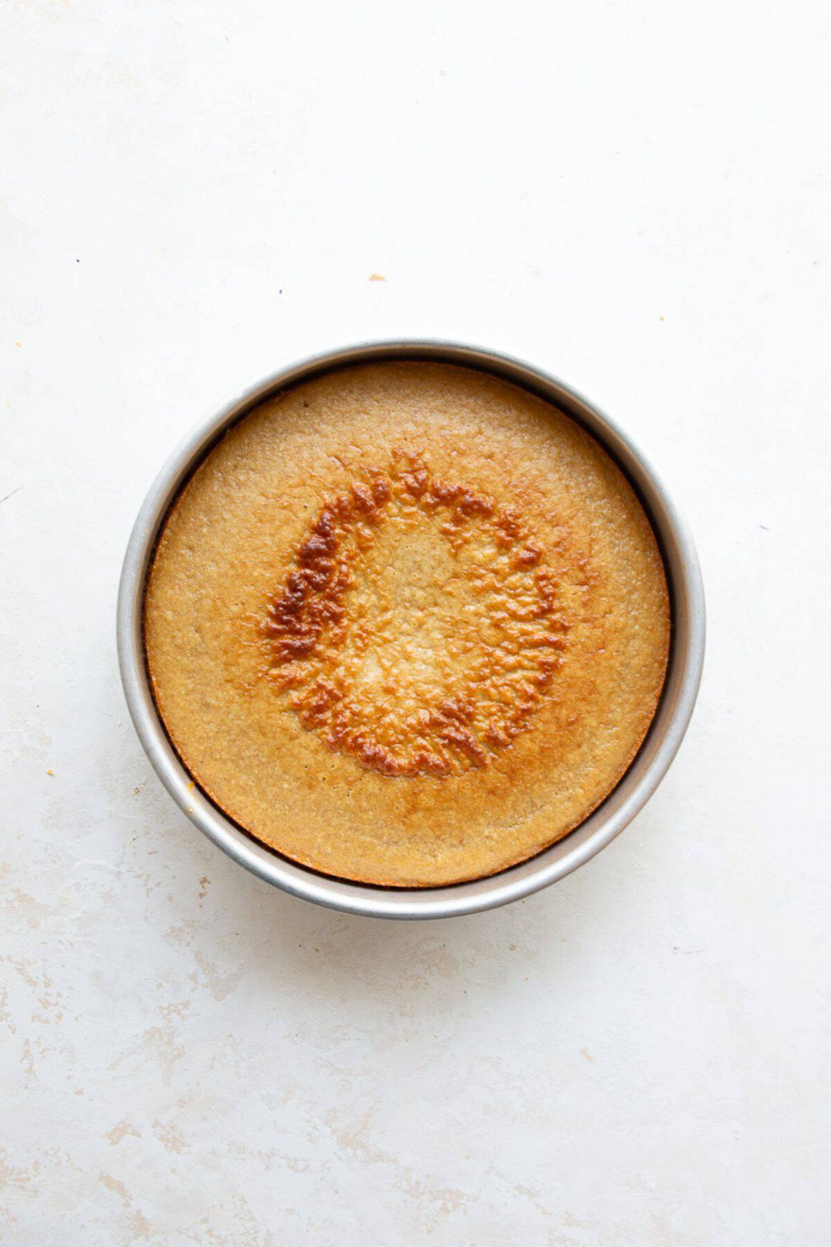 Golden baked protein cake cooling in a round metal cake pan.