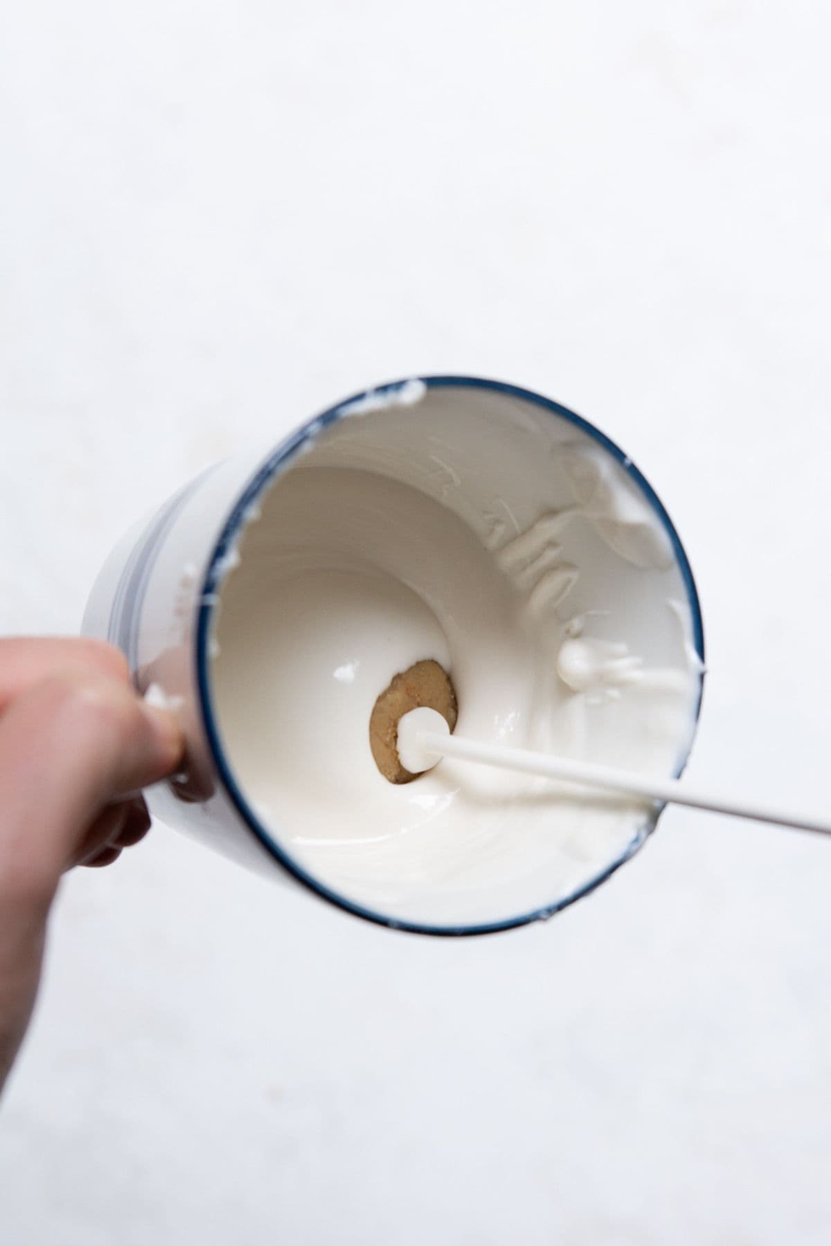 Dipping a cake pop stick into melted white chocolate before inserting it into a cake ball.