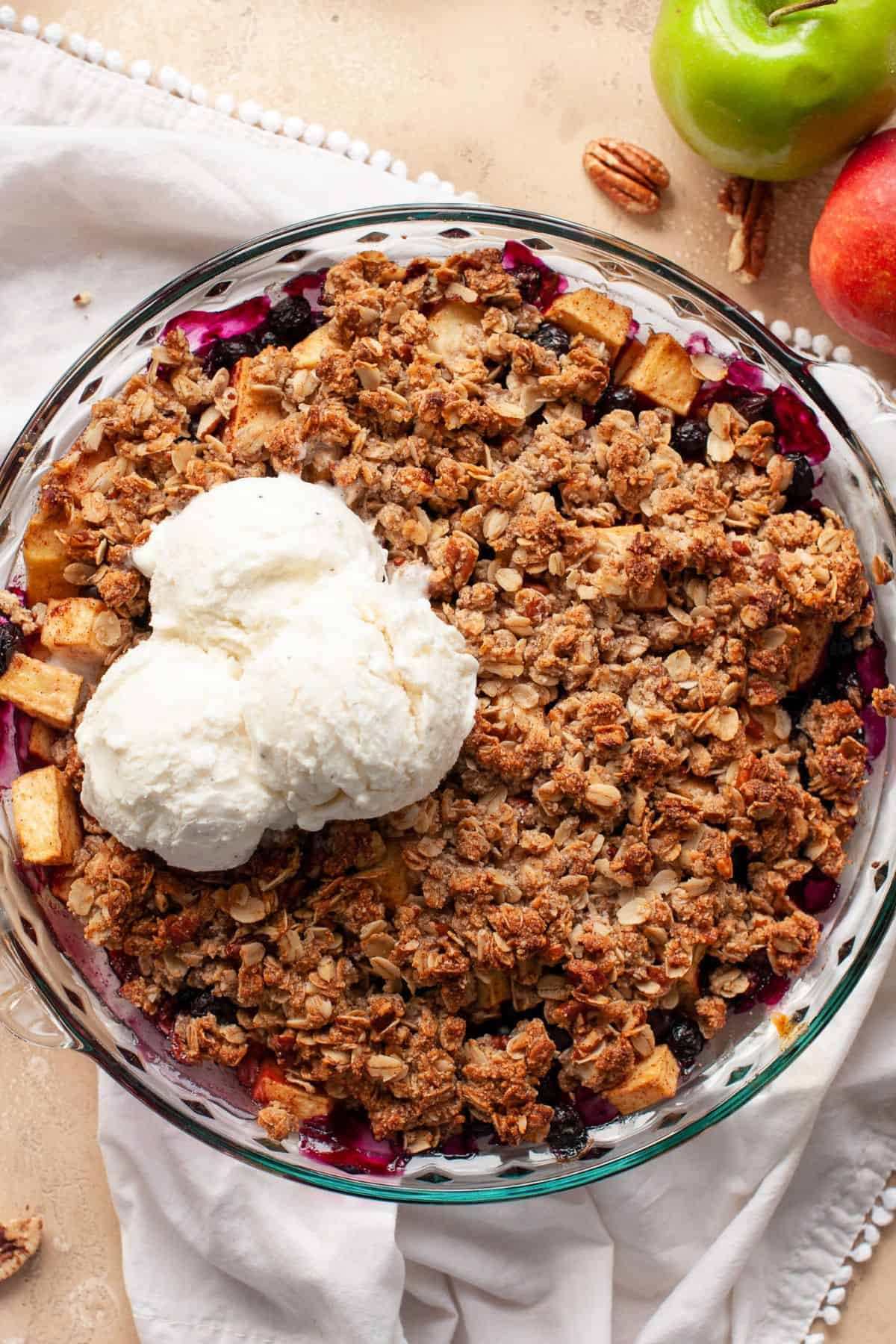 Baked apple blueberry crisp topped with two scoops of vanilla ice cream in a glass pie dish.