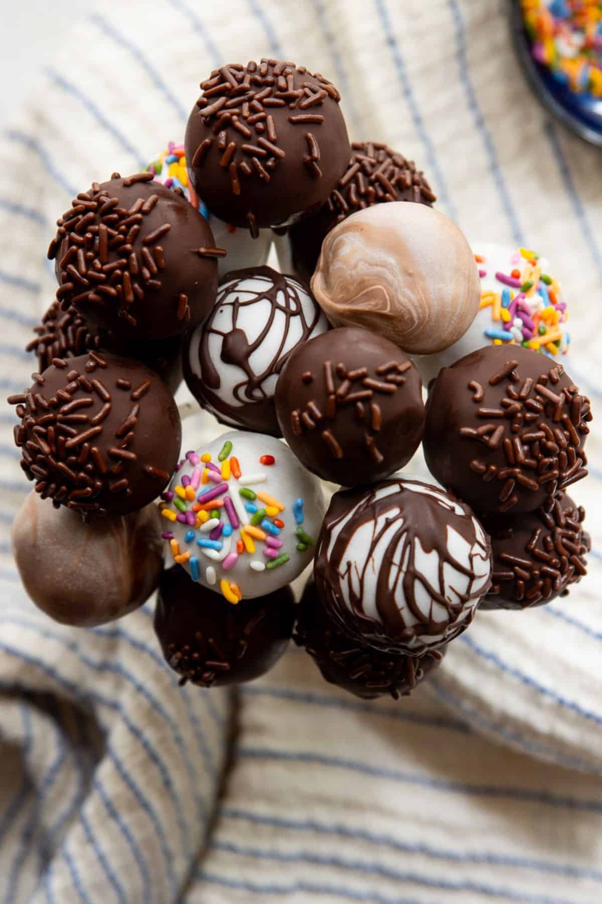 High-protein cake pops arranged in a bunch, dipped in dark chocolate, white chocolate, and marbled peanut butter with sprinkles.