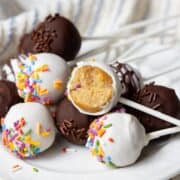 Healthy protein cake pops coated in white and dark chocolate with rainbow sprinkles, one bitten to show the soft vanilla center.