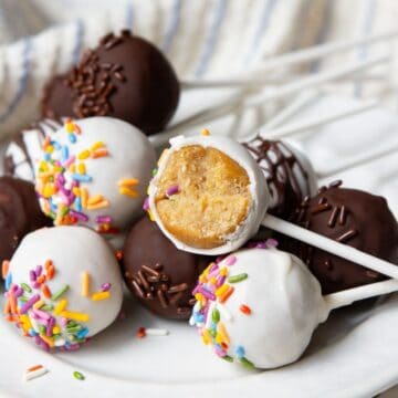 Healthy protein cake pops coated in white and dark chocolate with rainbow sprinkles, one bitten to show the soft vanilla center.