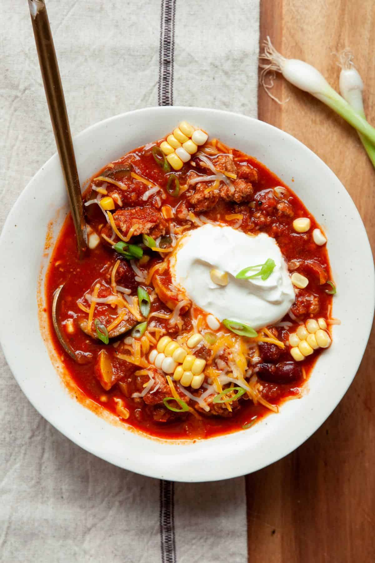 Healthy turkey chili in a bowl topped with Greek yogurt, corn, shredded cheese, and green onion.