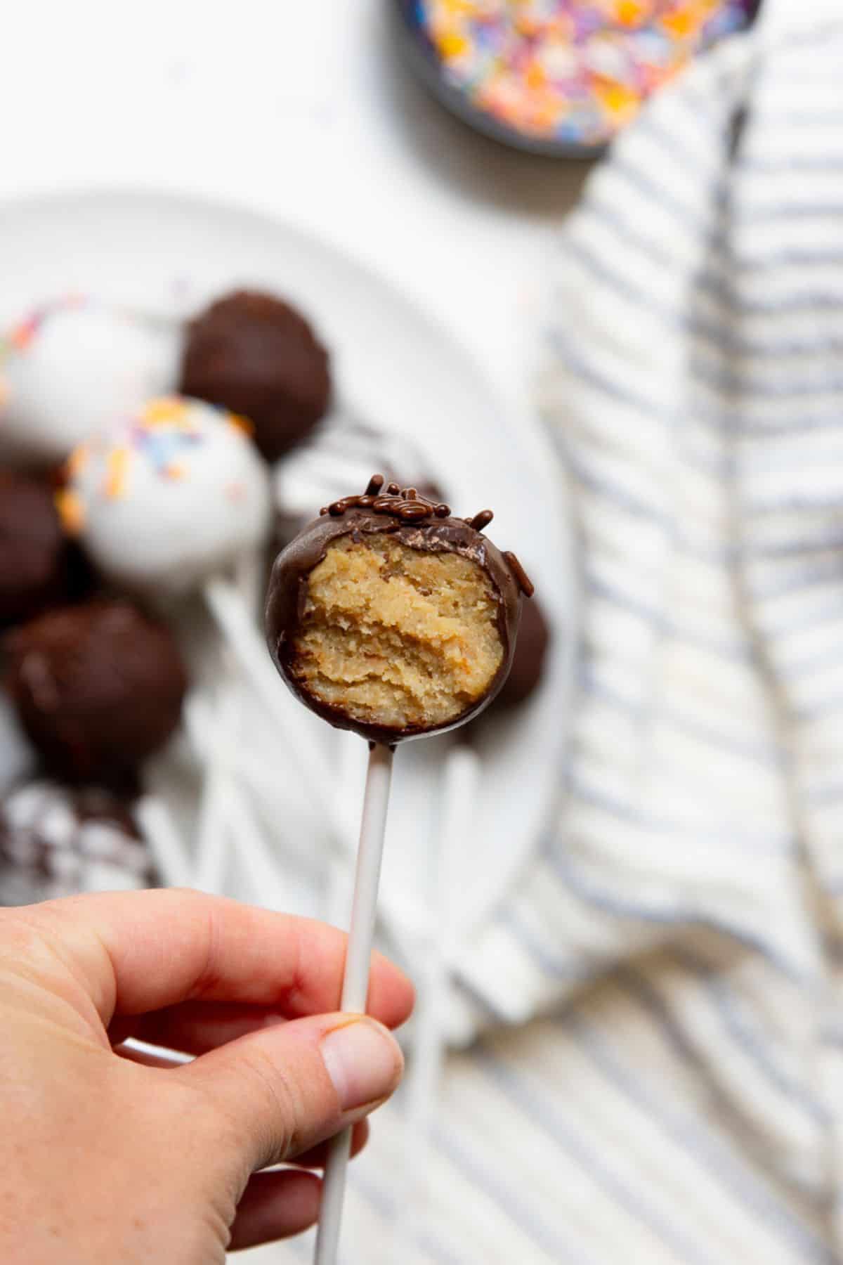 Hand holding a dark chocolate-dipped high-protein cake pop with a bite taken out, showing the peanut butter cake inside.