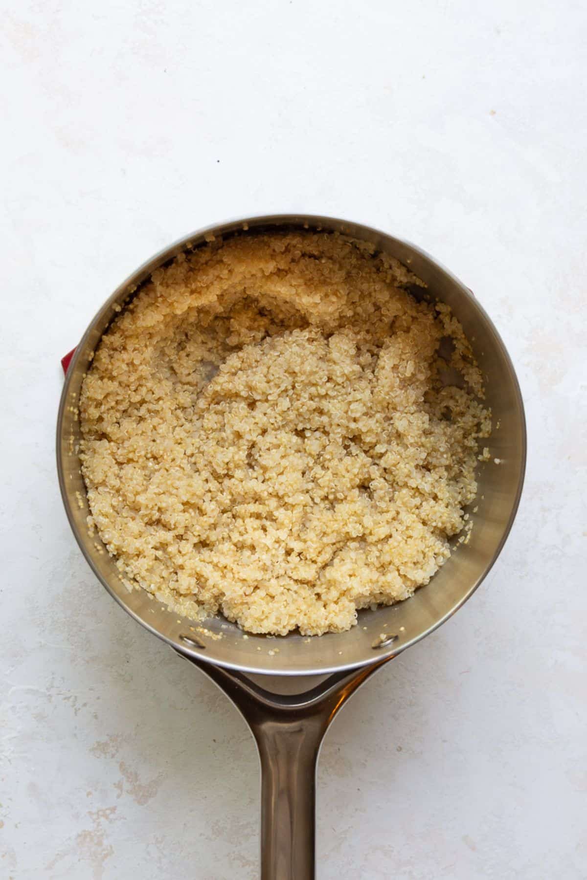 Cooked white quinoa with fluffy curly tails in a stainless steel saucepan.