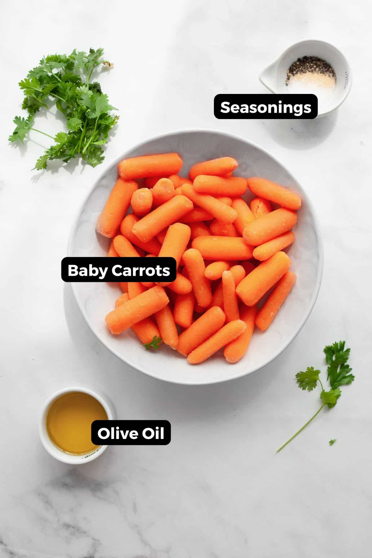 Ingredients in air fried baby carrots in small bowls, including: baby carrots, olive oil, salt, pepper, and garlic powder.