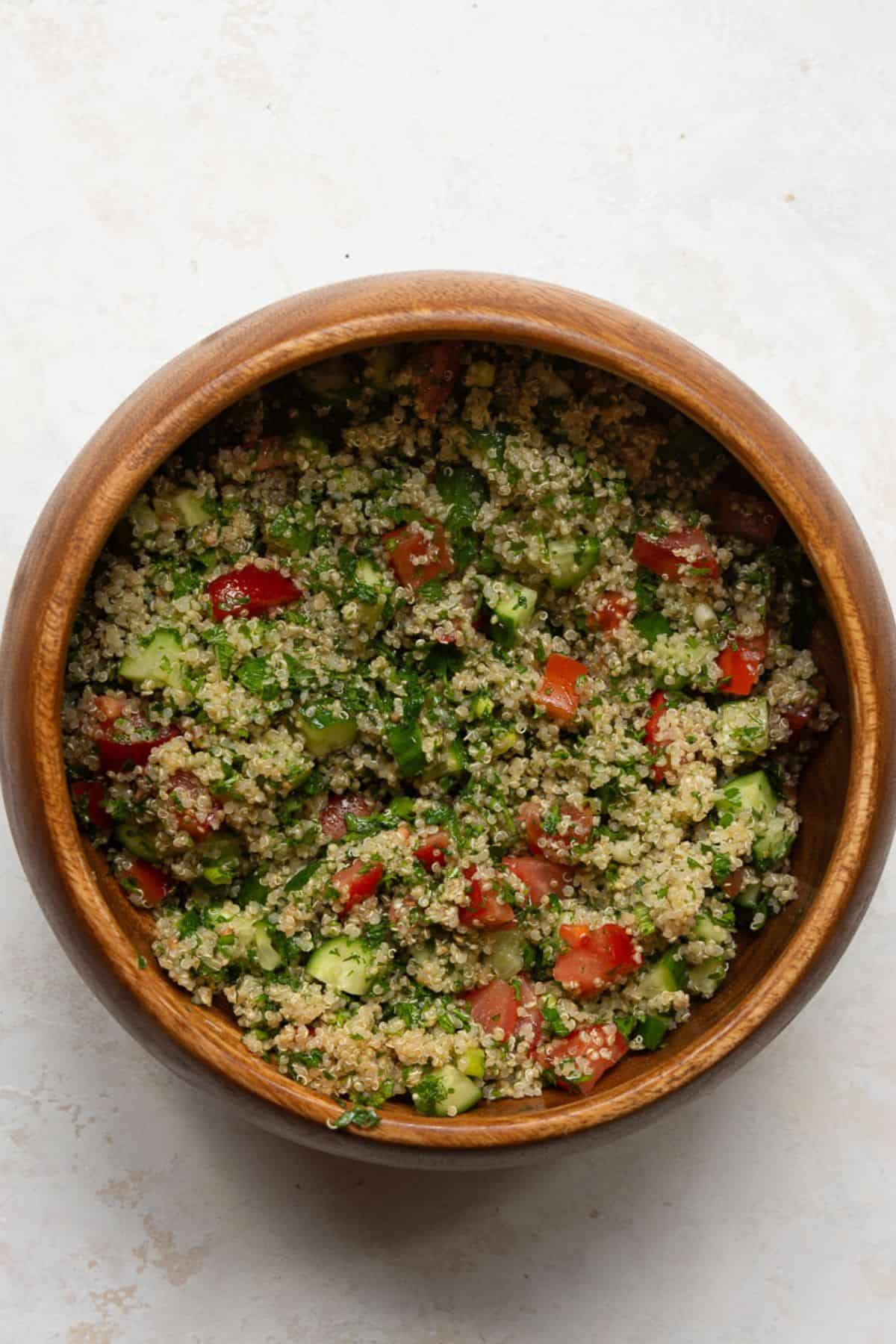 Mixed quinoa tabbouleh salad with parsley, tomato, and cucumber in a wooden bowl.