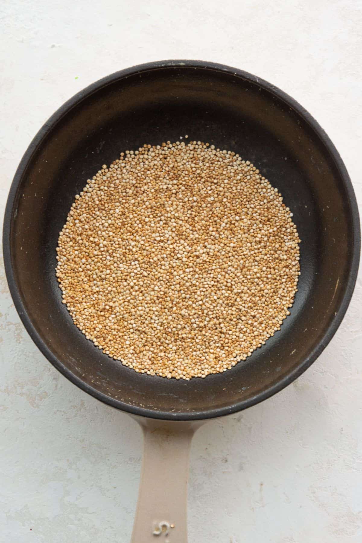 Raw white quinoa toasting in a dry black skillet until puffed and golden.