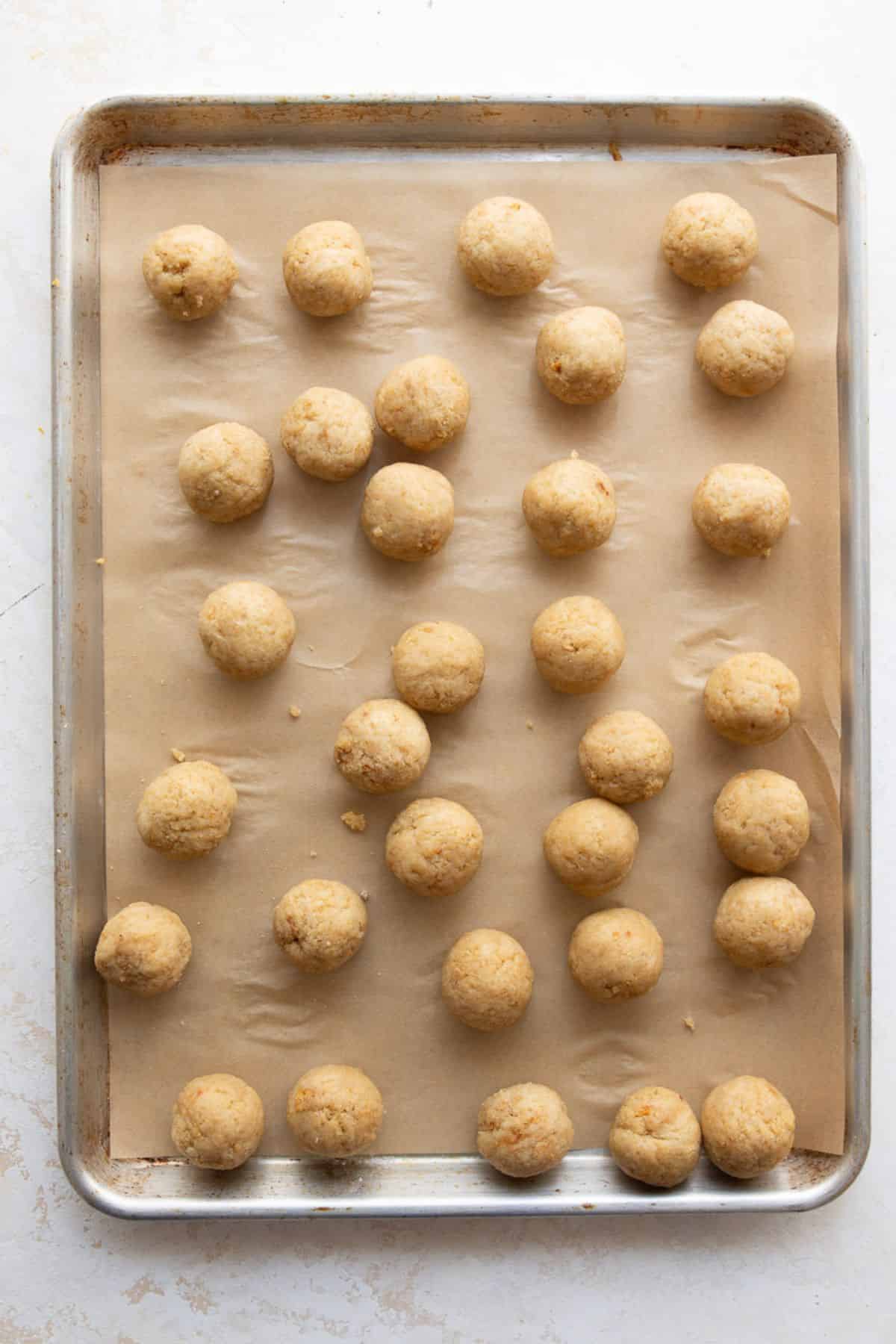 Rolled protein cake balls lined up on a parchment-lined baking sheet before chilling.