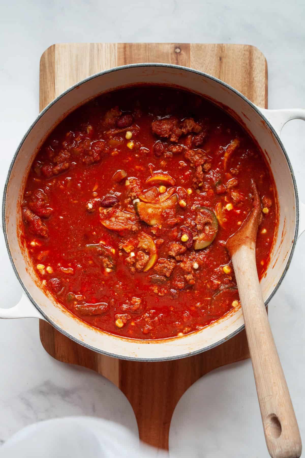Healthy turkey chili simmering until thickened in a white Dutch oven on a wood board.