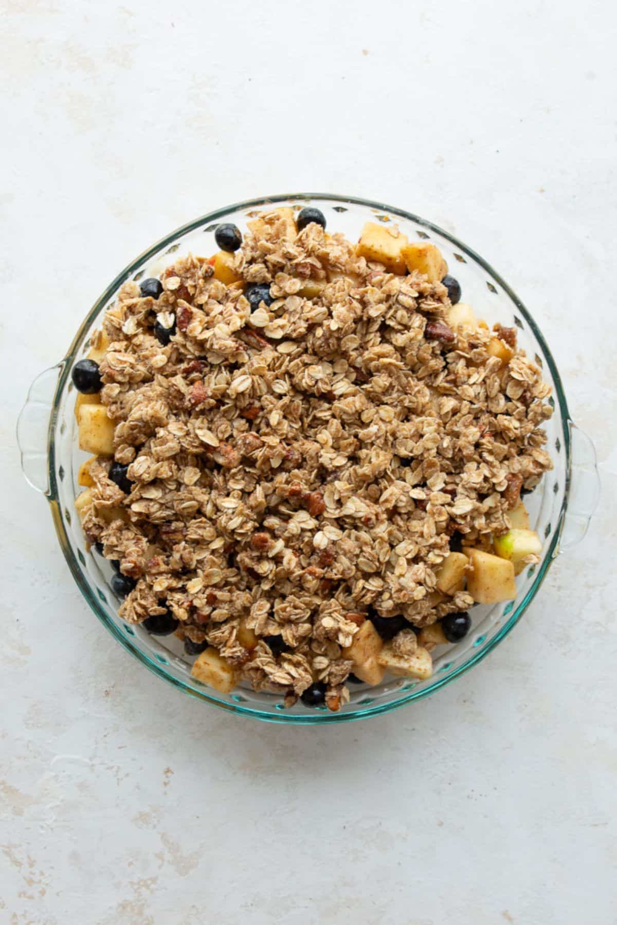 Unbaked apple blueberry crisp topped with almond flour oat crumble in a pie dish.