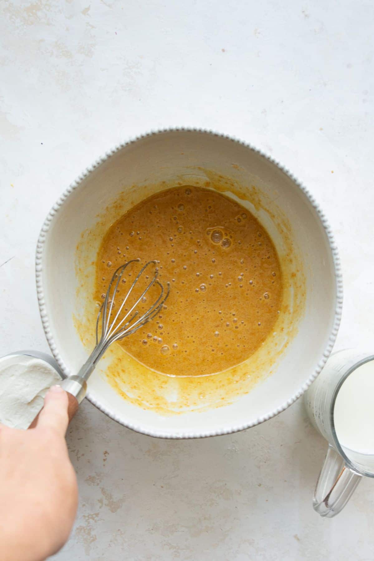Whisking eggs, sugar, and vanilla in a white bowl.