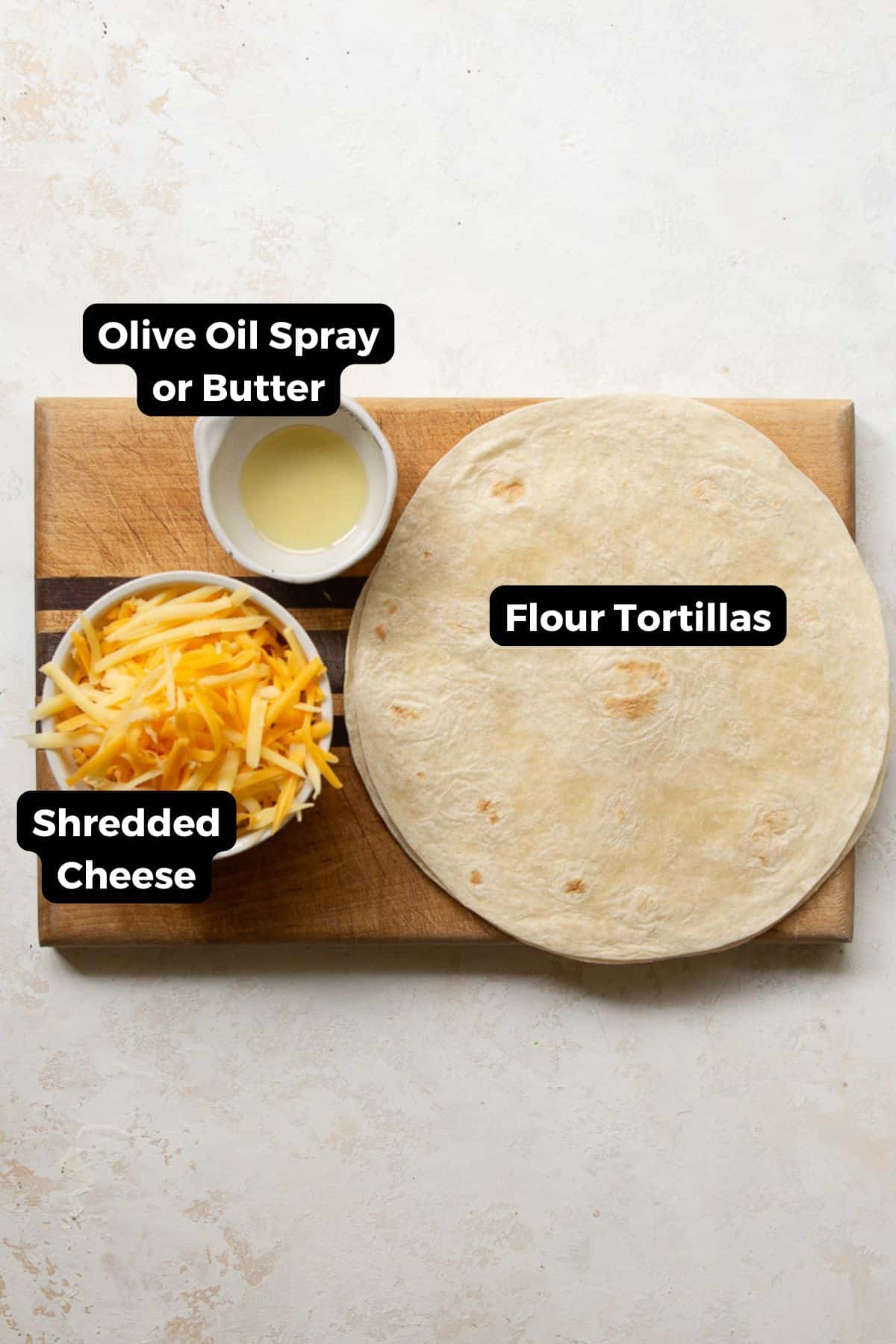 Flour tortillas, shredded cheddar cheese, and olive oil on a wooden cutting board with labels.