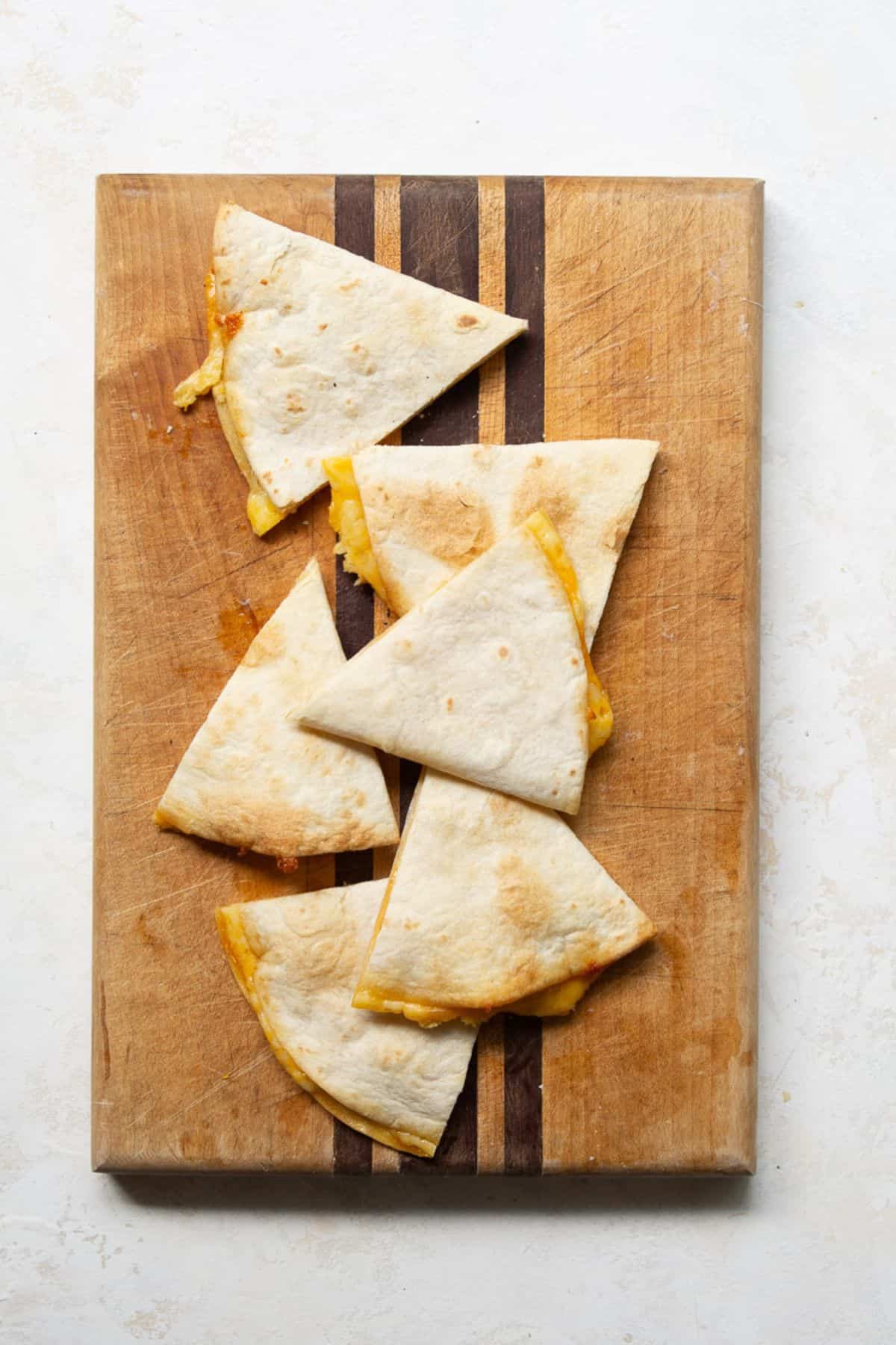 Cheese quesadilla cut into triangles on a wooden cutting board.