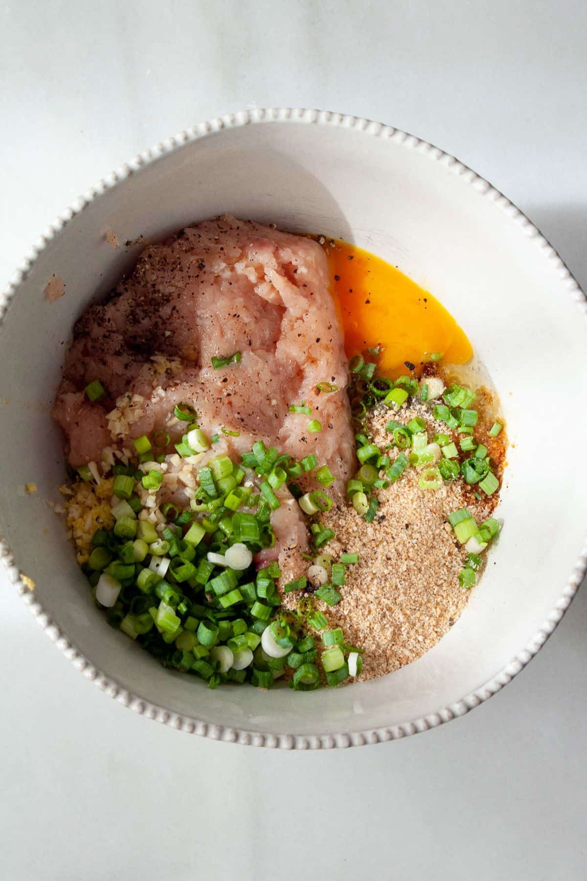 Ground chicken, egg, breadcrumbs, and green onion in a white mixing bowl.