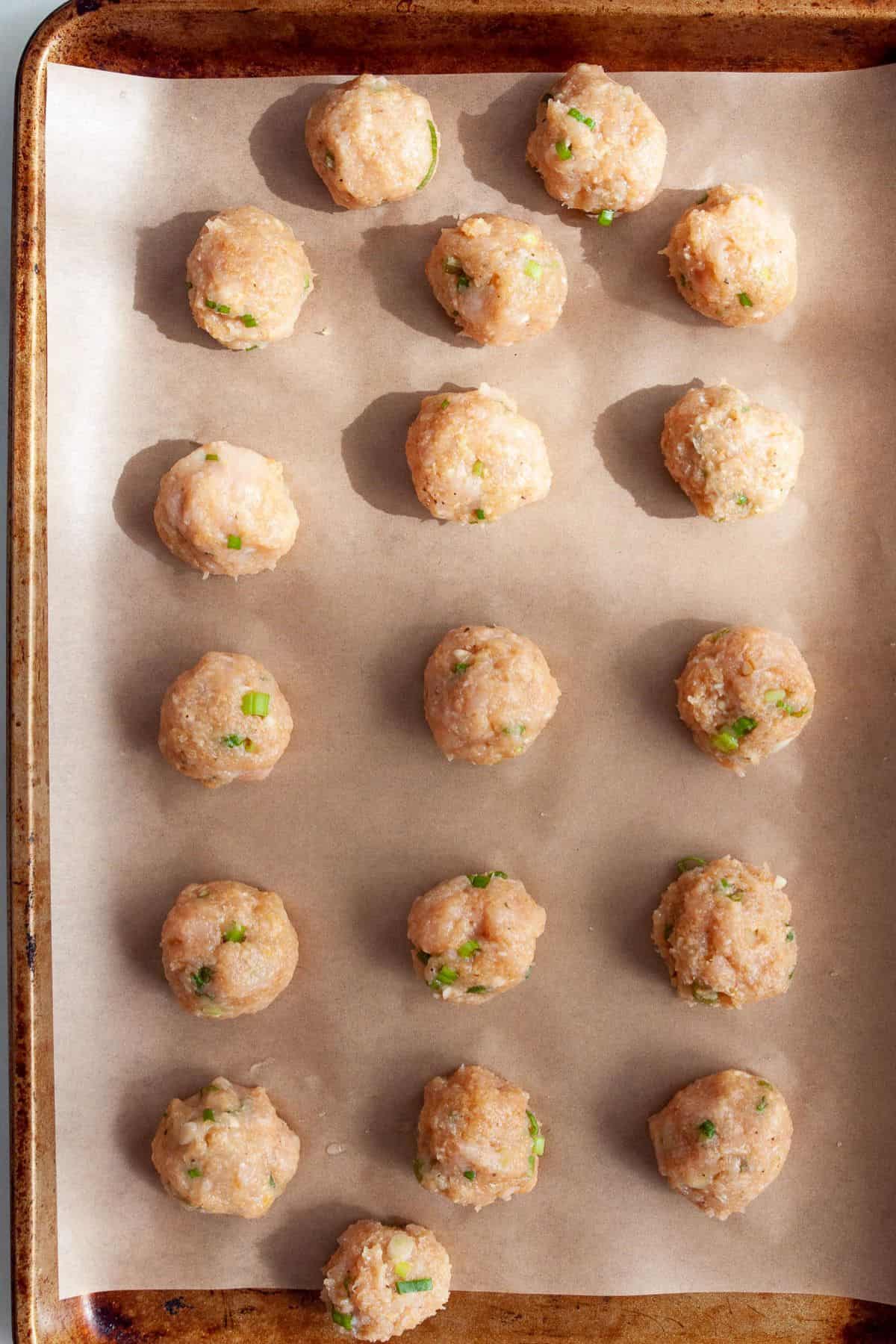 Rolled chicken meatballs spaced on a parchment lined baking sheet.