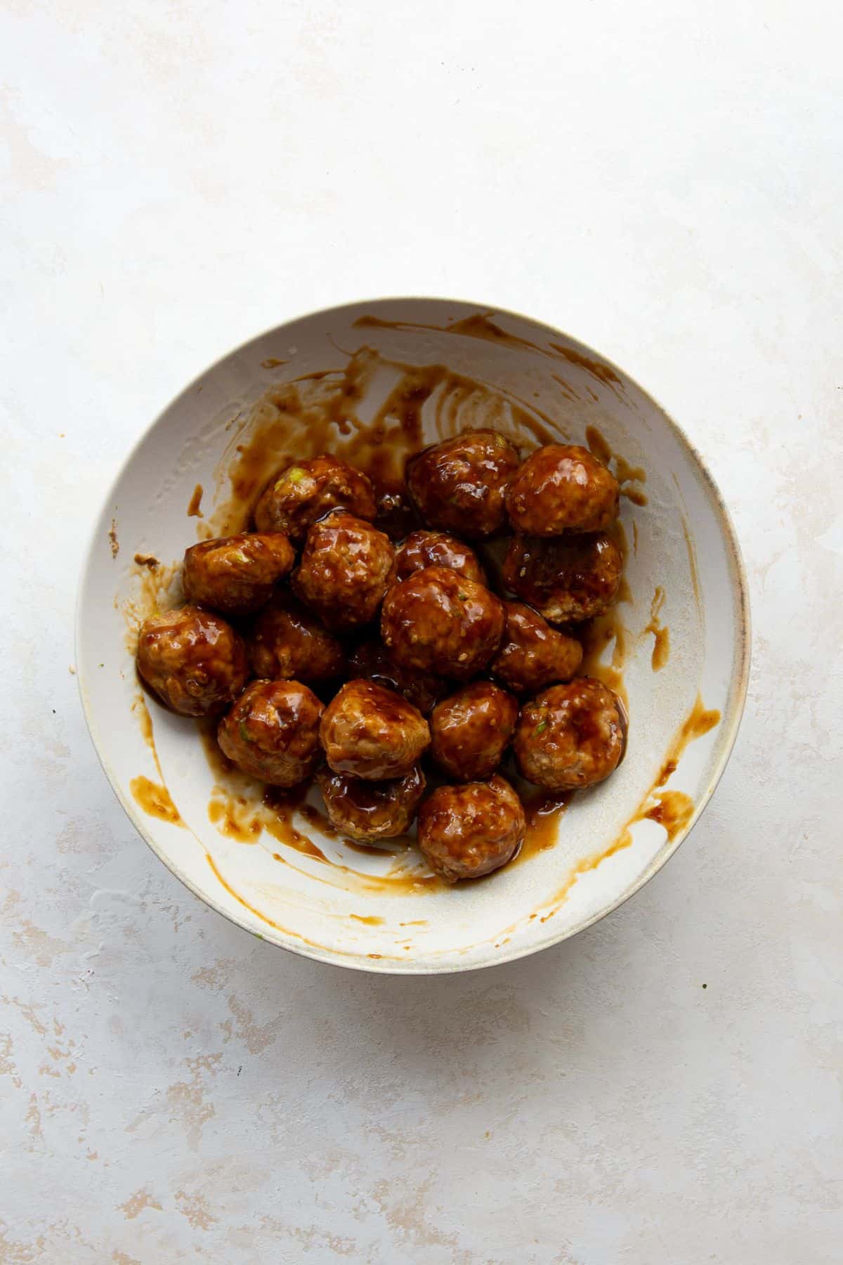 Baked chicken meatballs tossed in sticky sesame glaze in a bowl.