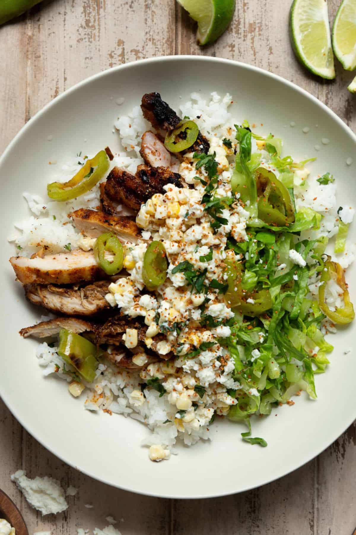 Assembled street corn chicken bowl with rice, sliced chicken, corn topping, romaine, and jalapeños.