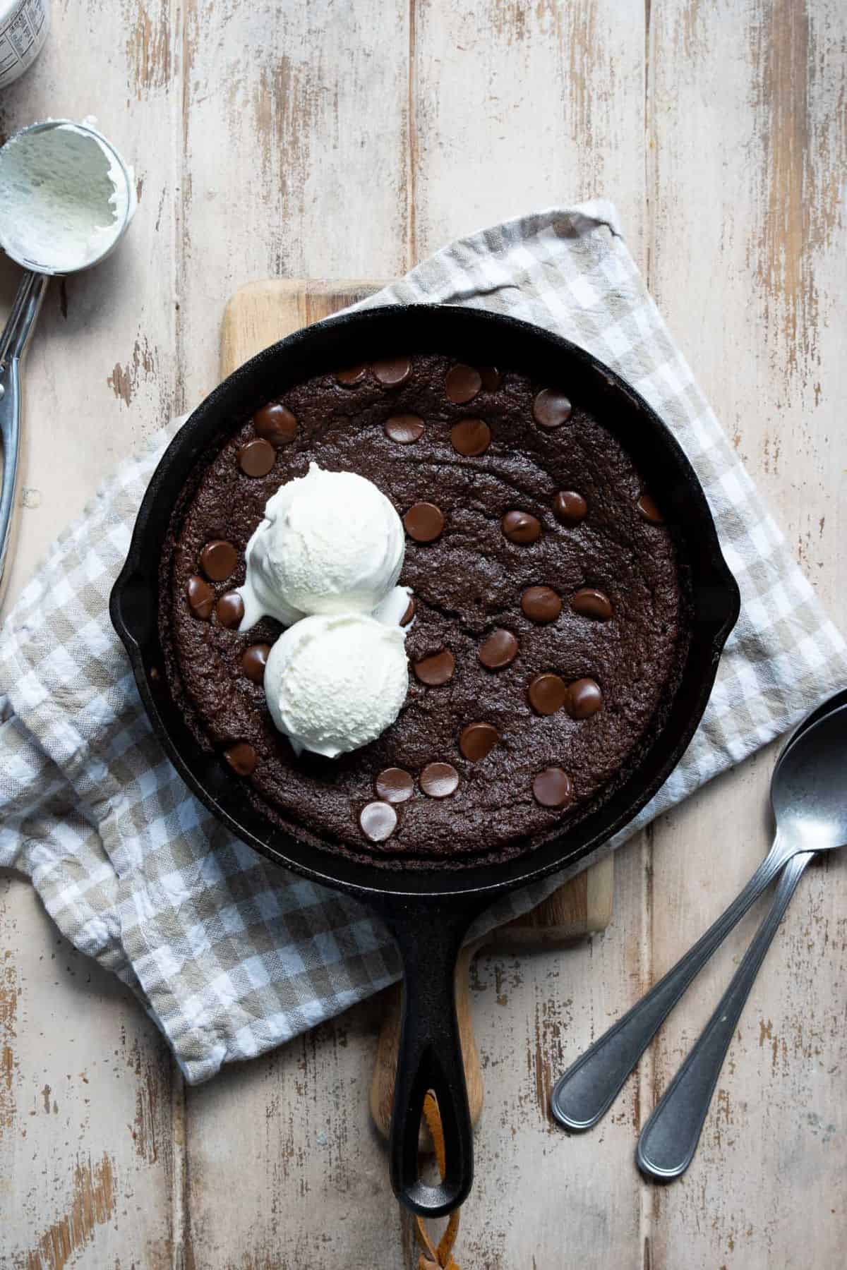 Baked flourless brownie skillet with a crackly top and two ice cream scoops on top.