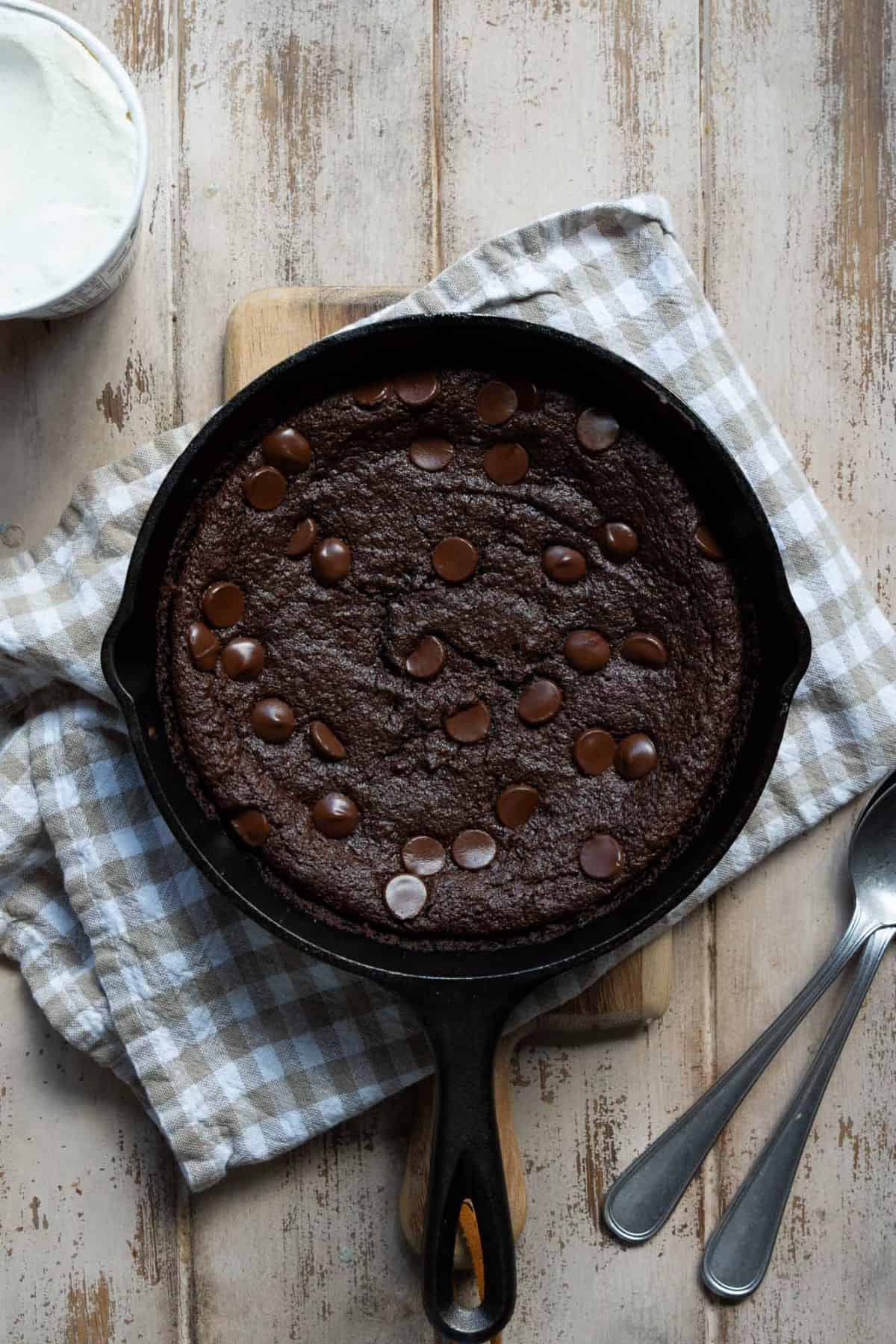 Baked flourless brownie skillet with a crackly top and melted chocolate chips.