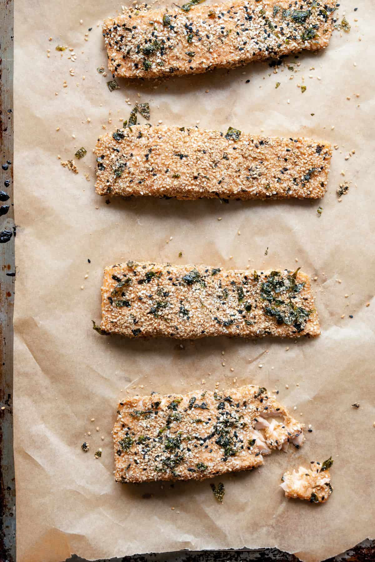 Four baked furikake salmon fillets on a sheet pan, one flaked open to show the cooked center.