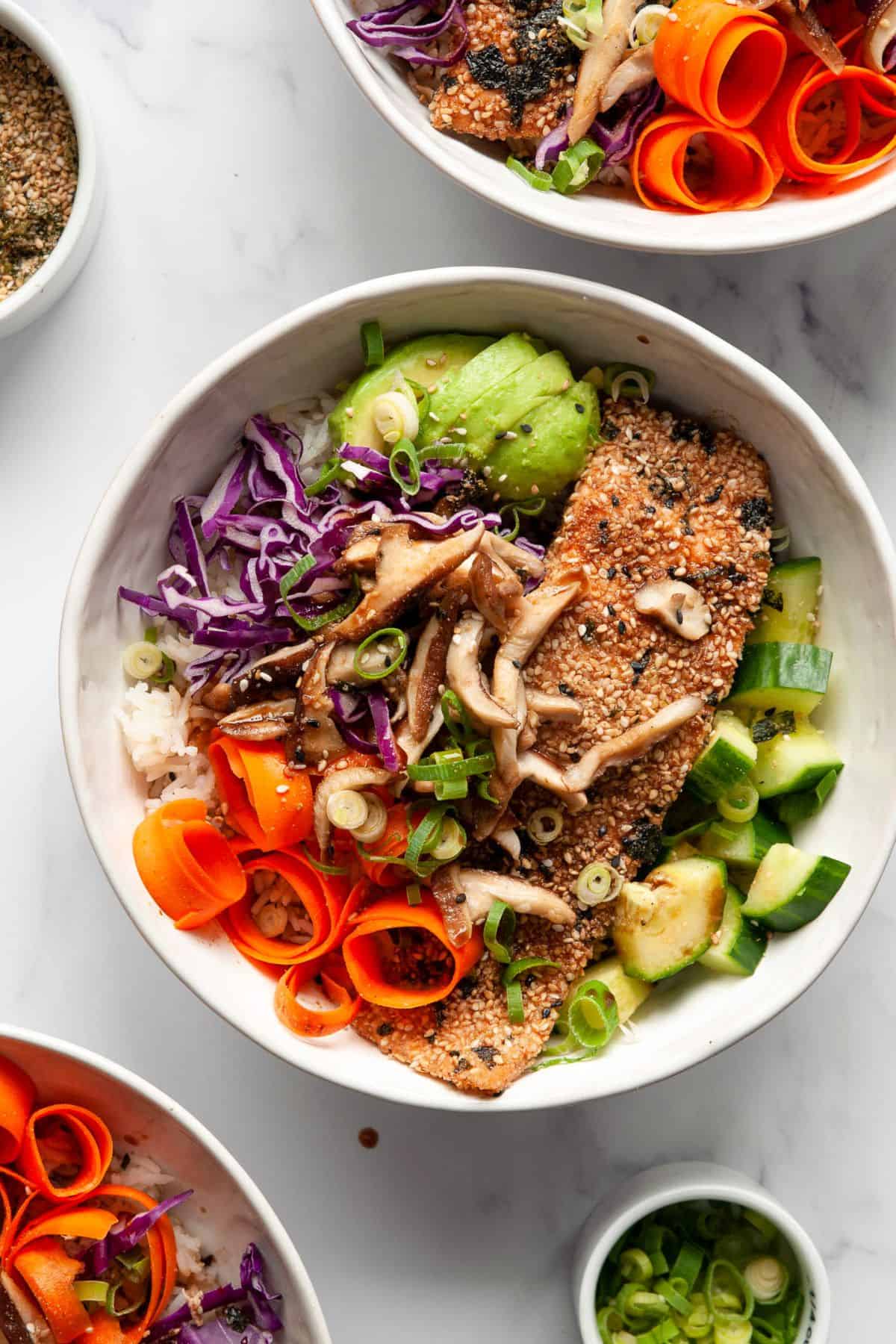 Baked furikake salmon over white rice with shiitake mushrooms, avocado, cucumber, carrot ribbons, and purple cabbage.