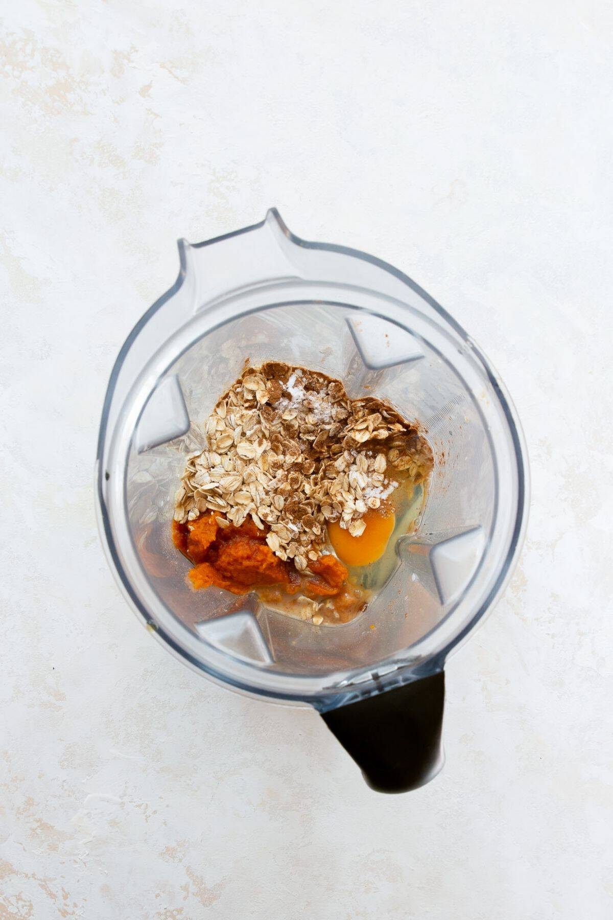 Rolled oats, pumpkin puree, an egg, and pumpkin pie spice in a blender before blending.