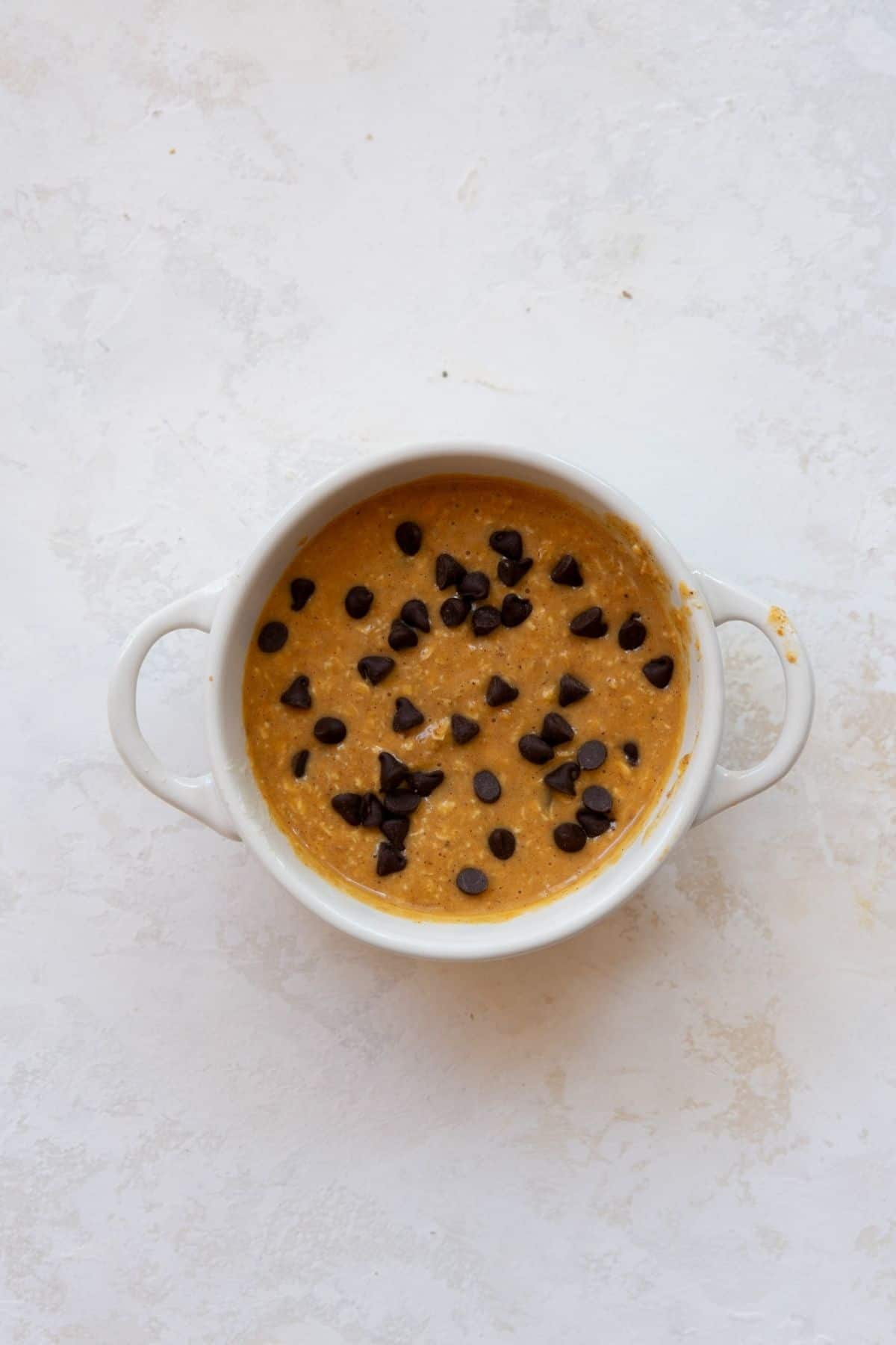 Unbaked pumpkin baked oats batter in a white ramekin topped with mini chocolate chips.