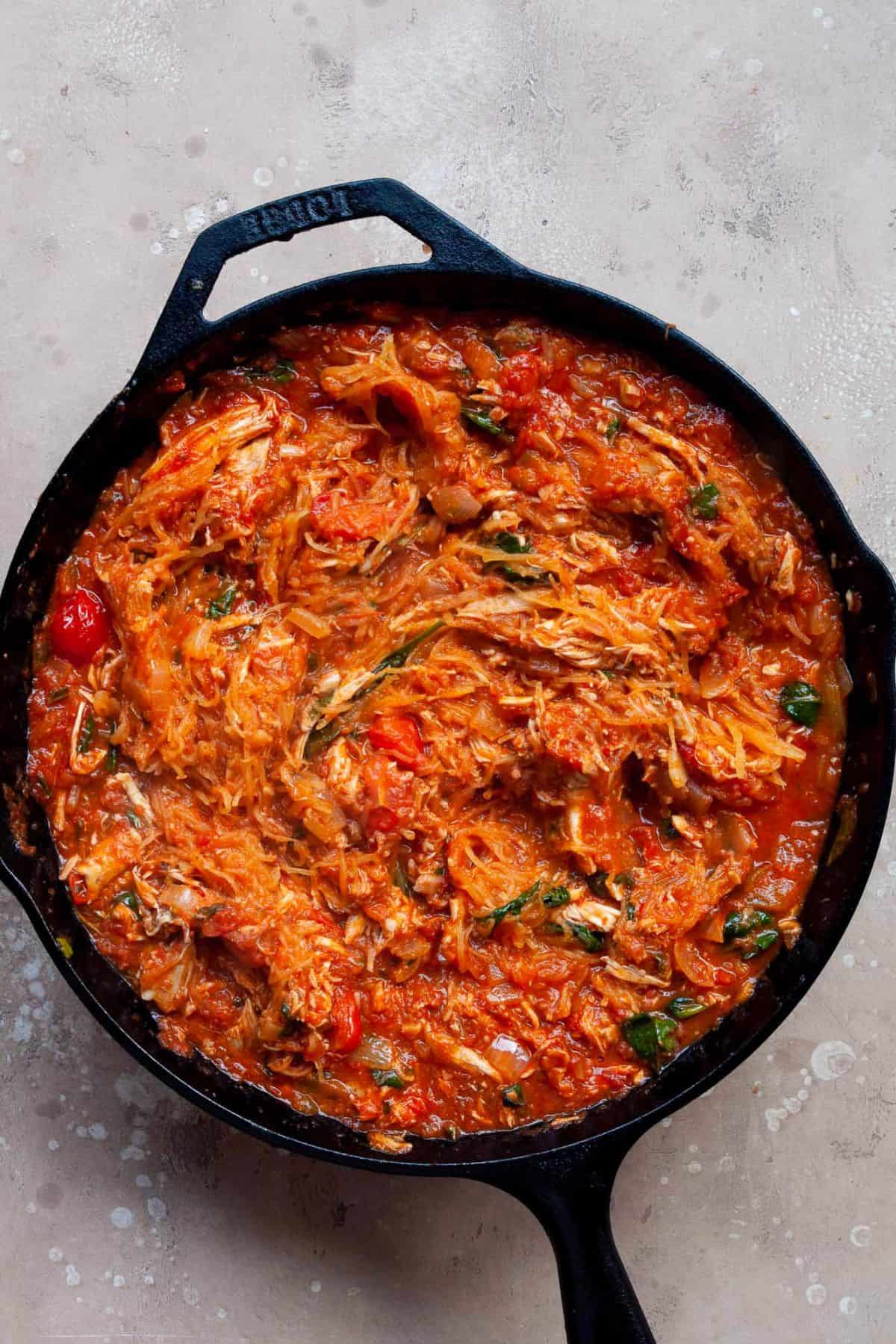 Chicken parmesan filling with shredded chicken, marinara, spinach, and basil in a cast iron skillet.