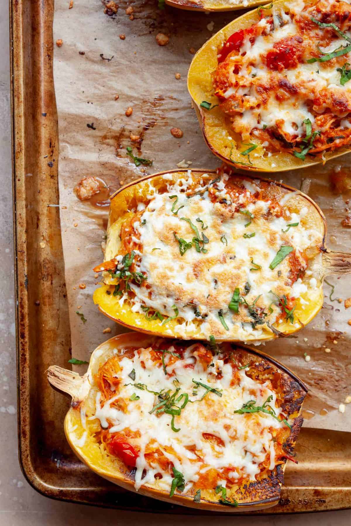 Chicken parmesan stuffed spaghetti squash boats with melted mozzarella and fresh basil on a baking sheet.