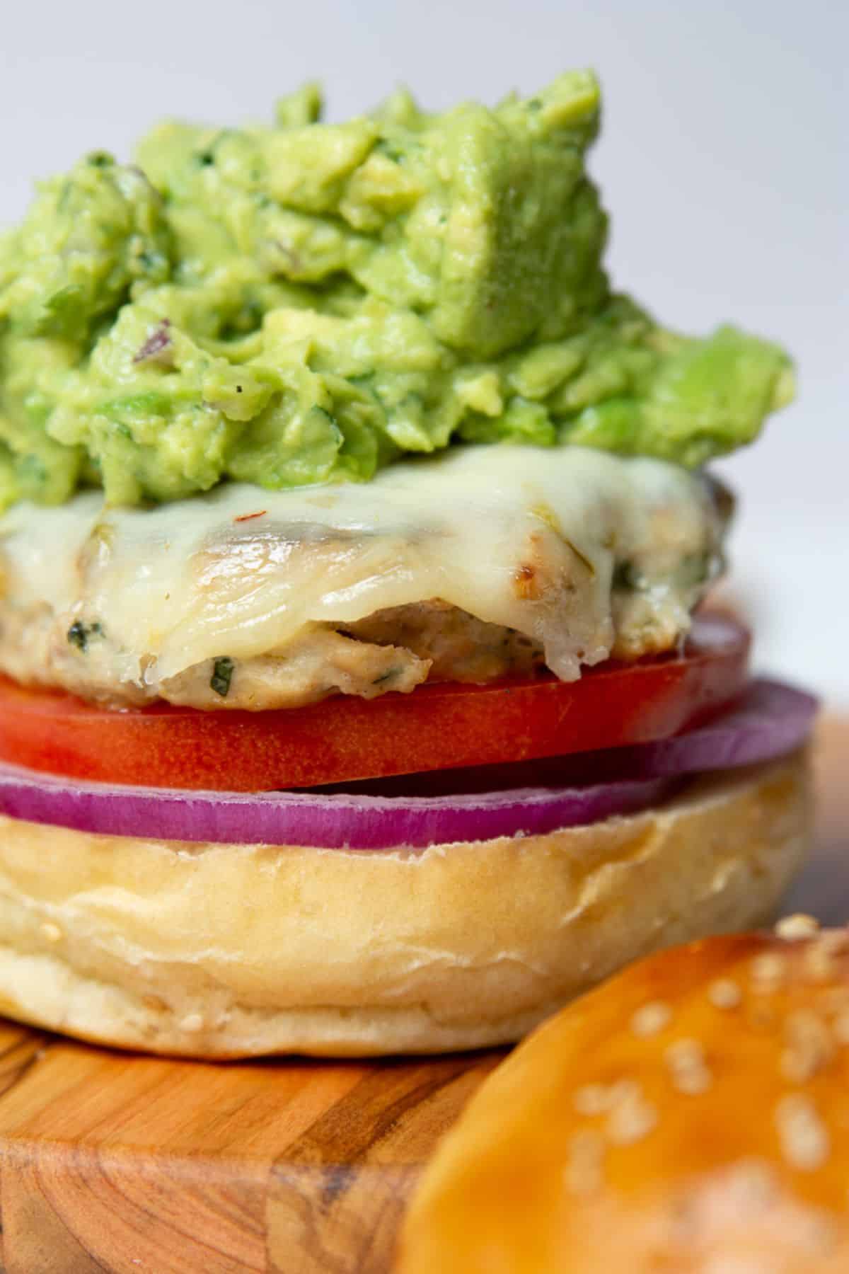Close up of a cilantro lime chicken burger topped with melted cheese and guacamole.