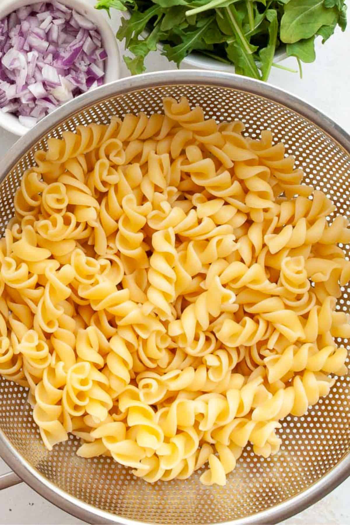 Cooked chickpea fusilli draining in a colander after rinsing under cold water.