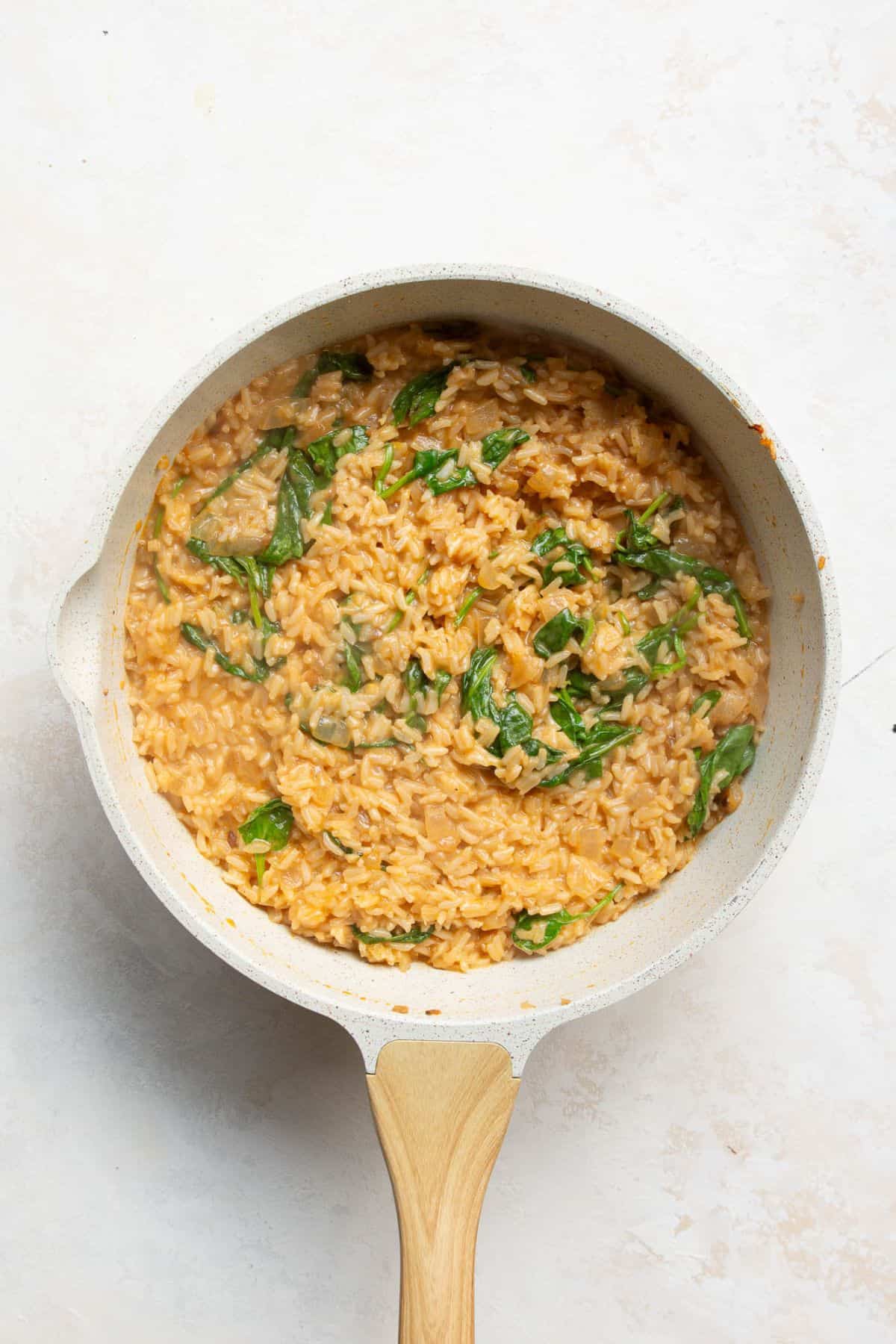 Creamy Greek lemon rice with wilted spinach stirred through in a skillet.
