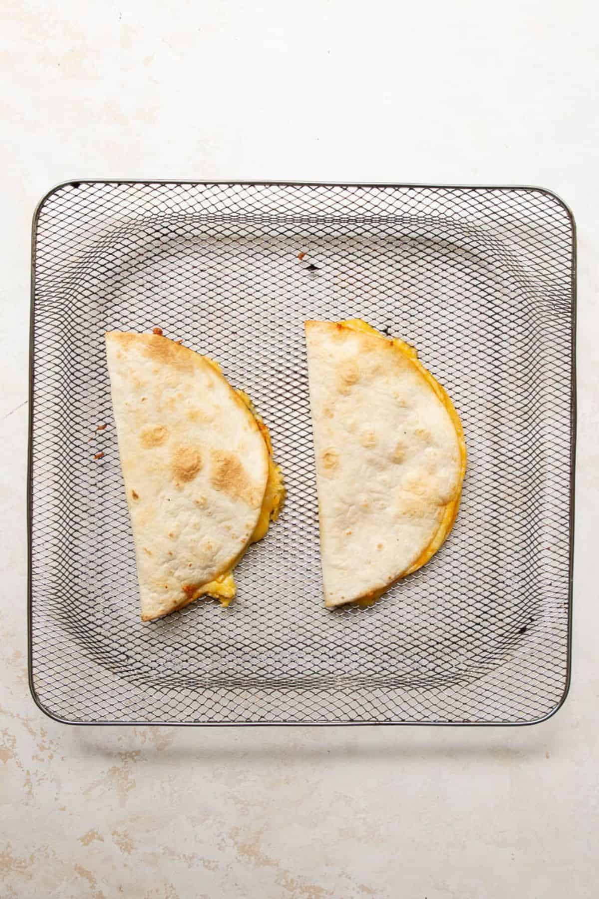 Two golden brown quesadillas in an air fryer basket after cooking.
