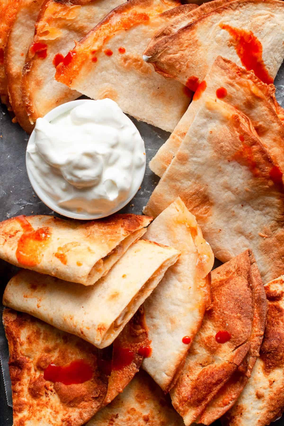 Crispy air fryer quesadilla wedges drizzled with hot sauce beside sour cream.