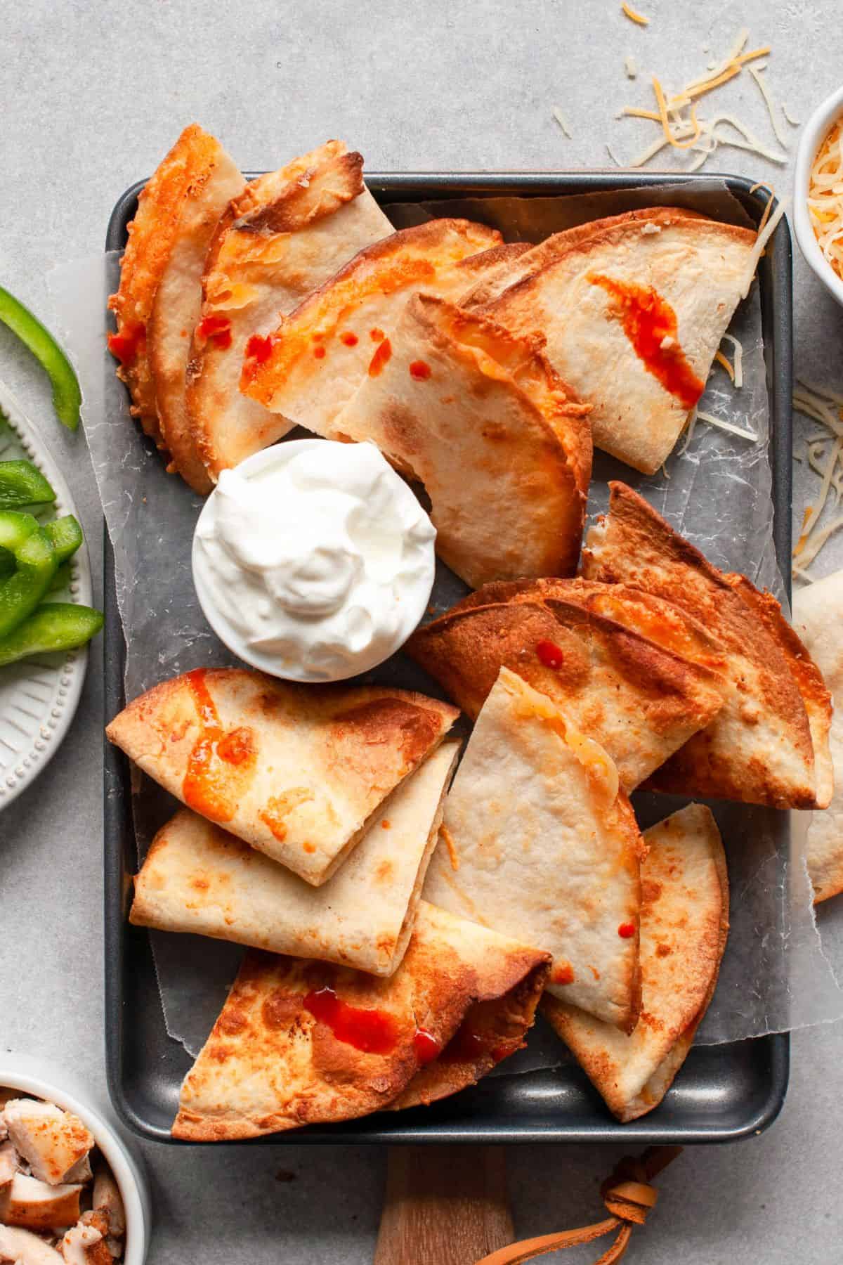 Chicken and cheese quesadilla wedges on a tray with sour cream, green peppers, and shredded cheese.