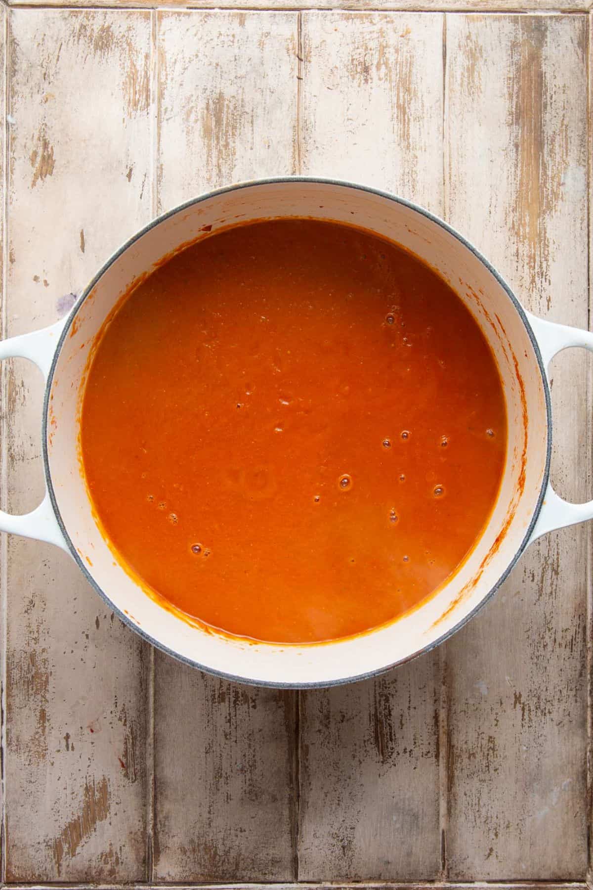 Creamy dairy free tomato soup in a white Dutch oven after stirring in the coconut milk.